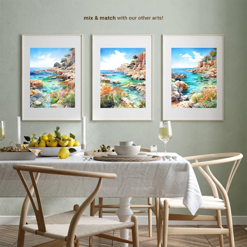 May include: Three framed watercolor paintings of a coastal scene with turquoise water, rocky cliffs, and lush greenery. The paintings are displayed on a light green wall above a dining table with a white tablecloth, wooden chairs, and a bowl of lemons.