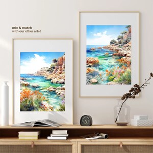 May include: Two framed watercolor paintings of a rocky coastline with turquoise water. The paintings are hanging on a white wall above a wooden shelf with books and a clock.