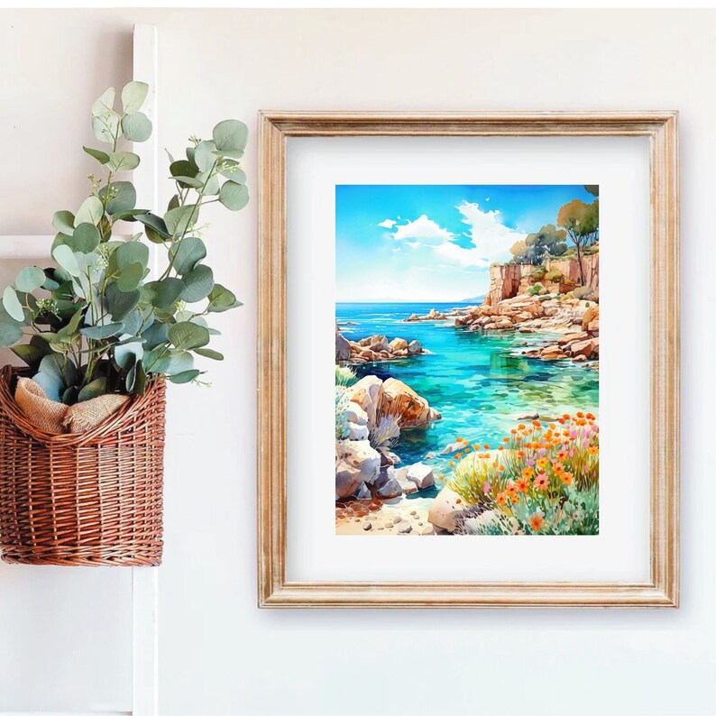 May include: A framed watercolor painting of a rocky coastline with turquoise water. The painting features a small cove with a sandy beach and lush green vegetation. The sky is blue with white clouds.