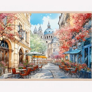 May include: A watercolor painting of a European street scene with a cafe on a cobblestone street. The cafe has red chairs and tables under yellow umbrellas. The street is lined with buildings and trees. A large blue domed church is in the background.