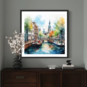 May include: Watercolor painting of a canal scene in Amsterdam, Netherlands. The painting features a narrow canal with buildings lining the sides, a bridge, and two boats. The buildings are painted in a variety of colors, including red, yellow, and blue. The boats are painted in a dark blue and red. The water is painted in a light blue color. The painting is framed in a black frame.