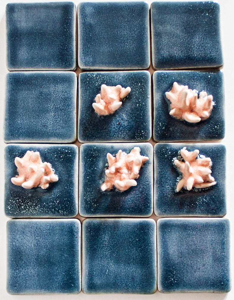 May include: A grid of twelve square ceramic tiles. Nine tiles are a textured, deep blue color. Three tiles feature a raised, coral-like design in a light peach color. The tiles are arranged in a 3x4 pattern.