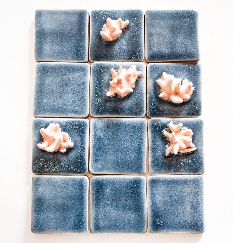 May include: A collection of twelve square ceramic tiles. Each tile is a deep blue with a textured surface. Some tiles feature a coral-like, light pink embellishment. The tiles are arranged in a grid pattern.