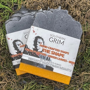 May include: Two handmade soaps with a black top and orange bottom, labeled "Southern Grim." The labels feature a horror movie character and the text "The Shape, Fresh Pumpkin, Green Leaves." Each soap weighs between 2.70-4.75 ounces.