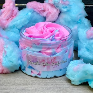 May include: A clear plastic jar filled with pink and blue whipped cream, surrounded by cotton candy. The jar has a label that reads "Kenneth's Cotton Candy Cloud". The cotton candy is pink and blue, and the background is a dark wood.