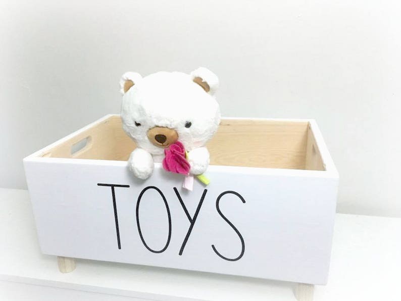 May include: White wooden toy storage box with a white plush bear holding a pink flower. The box has the word "TOYS" written on the front in black.