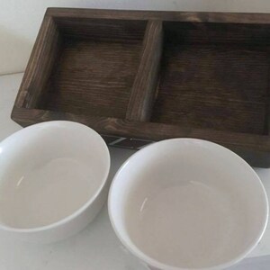Puede incluir: Dos cuencos de cer&aacute;mica blanca colocados sobre una bandeja de madera con un compartimento dividido. La bandeja es de color marr&oacute;n oscuro y tiene una veta de madera natural.