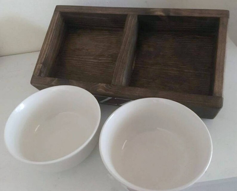 Puede incluir: Dos cuencos de cer&aacute;mica blanca colocados sobre una bandeja de madera con un compartimento dividido. La bandeja es de color marr&oacute;n oscuro y tiene una veta de madera natural.