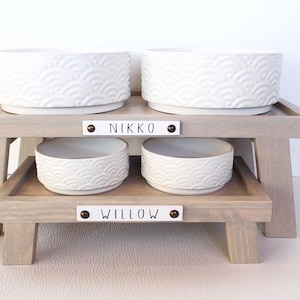 May include: Two raised dog food and water bowls with the names "Nikko" and "Willow" on the wooden stands.
