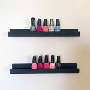May include: Two black floating shelves with nail polish bottles in various colors, including pink, red, blue, and silver.