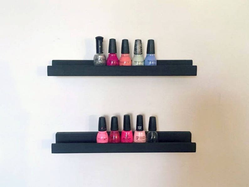 May include: Two black floating shelves with nail polish bottles in various colors, including pink, red, blue, and silver.