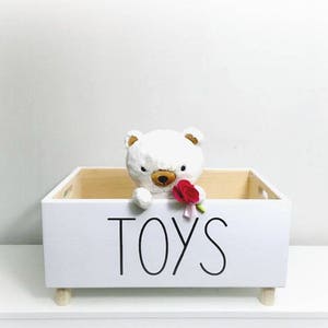 May include: White wooden toy storage box with a white teddy bear holding a red rose. The box has the word "TOYS" written on the front in black.