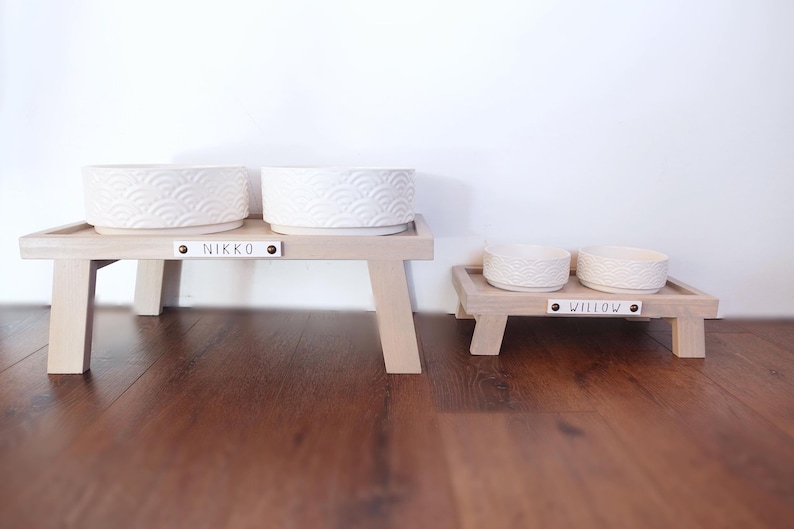 May include: Two elevated dog bowls with a white ceramic finish and a wave pattern. The larger bowl set is labelled "NIKKO" and the smaller set is labelled "WILLOW".