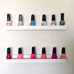 May include: Two white shelves with a variety of nail polish bottles in different colors, including pink, red, blue, and green.