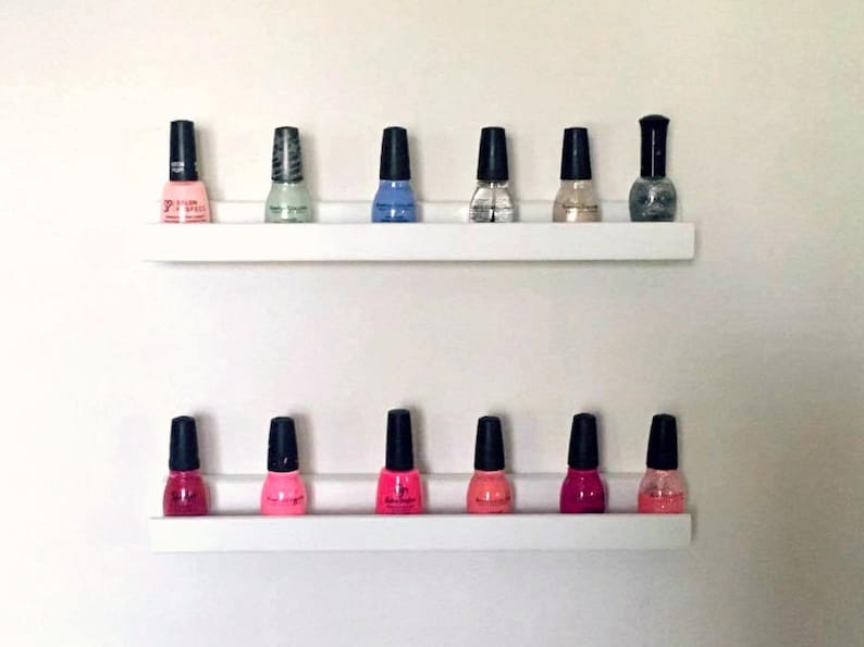 May include: Two white shelves with a variety of nail polish bottles in different colors, including pink, red, blue, and green.