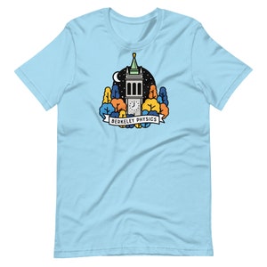 May include: Light blue t-shirt featuring a graphic of a clock tower surrounded by trees and a night sky. The text "Berkeley Physics" is displayed on a banner below the tower. The shirt is made of a soft material.