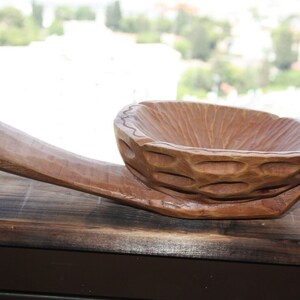 Op de afbeelding: Een houten kom met een uniek, getextureerd ontwerp. De kom heeft een handvat en is gegraveerd om op een schelp te lijken.
