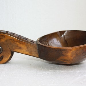 Op de afbeelding: Een houten kom met een gegraveerd handvat. De kom is bruin en heeft een gladde afwerking. Het handvat is ook bruin en heeft een gegraveerd ontwerp.