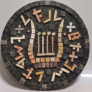 Pode incluir: Uma obra de arte circular em mosaico com um fundo preto e um desenho central de lira feito de azulejos de cor castanho claro, bege e branco. A lira é rodeada por uma borda de azulejos pretos, castanhos e bege dispostos em um padrão geométrico.