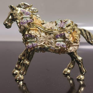 May include: A gold-colored horse figurine with a detailed design of butterflies in various colors, including purple, pink, and yellow. The figurine is a decorative trinket box.