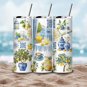 Può includere: Tre bicchieri cilindrici con coperchi e cannucce argentate, caratterizzati da uno sfondo bianco decorato con illustrazioni mediterranee blu e gialle di alberi di limoni, vasi in ceramica, brocche, tazze da caffè e balconi costieri.