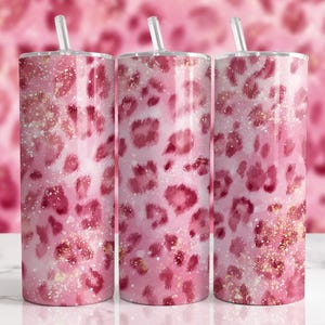 May include: Three tall, cylindrical tumblers with lids and straws. The tumblers feature a pink leopard print design with gold glitter accents. The background is a blurred pink leopard print.
