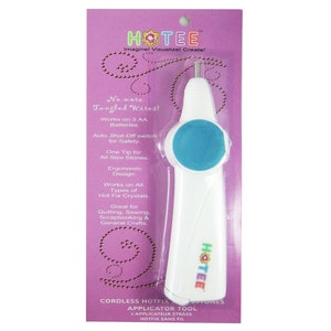 May include: A white and blue cordless hotfix rhinestone applicator tool packaged on a purple cardboard backing. The packaging features the text HOTEE, No more Tangled Wires!, Works on 3 AA Batteries, Auto Shut-Off switch, and CORDLESS HOTFIX RHINESTONES.