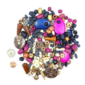 May include: A selection of mixed beads in diverse forms and hues. The beads are made from wood, stone, and metal, with shades of blue, pink, brown, black, and cream. A quarter and a penny are also visible.