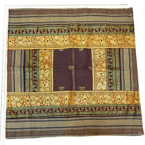 May include: A square textile featuring a central dark purple panel with thin horizontal stripes, surrounded by wide bands of gold floral patterns, green paisley borders, and outer sections of tan fabric with intricate geometric line details.