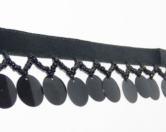 May include: Black sequin trim with a black ribbon base. The trim features a zig-zag pattern of black beads and dangling black sequins. This decorative trim is suitable for various craft and sewing projects.