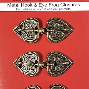 May include: Three sets of antique gold metal hook and eye closures in the shape of hearts with ornate designs.  Sew Trendz imagine! visualize! create! Metal Hook & Eye Frog Closures Fermetures à crochet et à oeil en métal