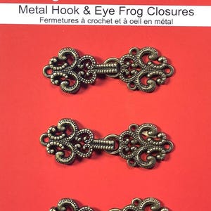 Peut inclure: Trois fermoirs à crochet et à oeil en métal de couleur or antique avec des motifs ornés.  Sew Trendz imagine! visualize! create! Metal Hook & Eye Frog Closures Fermetures à crochet et à oeil en métal