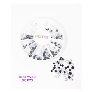 May include: A white circular plastic storage container with twelve divided compartments containing small clear round rhinestones. The center of the lid features the text HOTEE. A pile of loose clear rhinestones sits nearby with the text BEST VALUE 300 PCS.