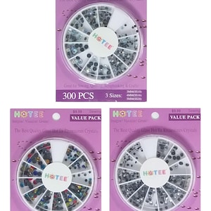 May include: Three purple packaging cards each containing a circular white plastic organizer filled with assorted glass hot fix rhinestones. The text on the cards reads HOTEE, Sewing Value Pack, 300 PCS, and lists three sizes: 3mm, 4mm, and 5mm.