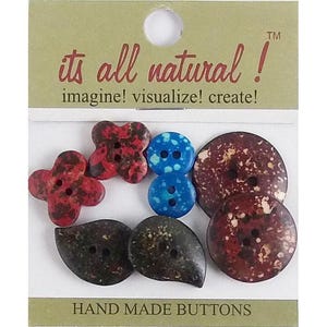 May include: A collection of assorted buttons on a display card labelled its all natural! imagine! visualize! create! and HAND MADE BUTTONS. The set includes two red floral-shaped buttons, two blue circular buttons, two dark teardrop-shaped buttons, and two large round buttons with a mottled red and brown pattern.
