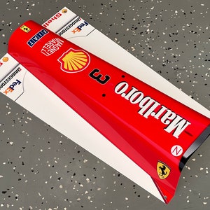 May include: A red and white race car nose cone with the Marlboro logo and the words "Marlboro" and "Shell" printed on it. The car also has the logos for FedEx, Bridgestone, and Fiat.