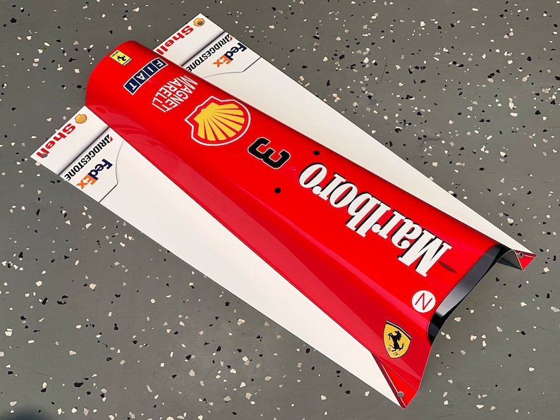 May include: A red and white race car nose cone with the Marlboro logo and the words "Marlboro" and "Shell" printed on it. The car also has the logos for FedEx, Bridgestone, and Fiat.