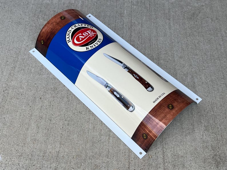 May include: A white and blue metal sign with a red Case Knives logo and two pocket knives. The sign reads "Hand-Crafted Case Knives" and "Made in USA".