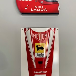 Peut inclure: Casque de course rouge et blanc avec le texte "GOOD YEAR" et "NIKI LAUDA" sur le côté. Un nez de voiture de course rouge et blanc avec le texte "HEUER", "Agip" et "GOOD YEAR" dessus. Le numéro "1" est sur le devant du nez.