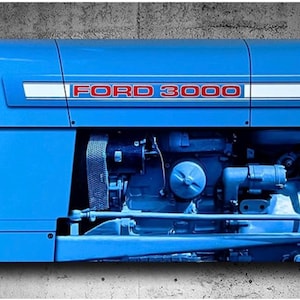 May include: A close-up of a blue Ford 3000 tractor. The tractor's hood features the text "FORD 3000" in red lettering. The engine and other mechanical components are visible, painted in a matching blue.