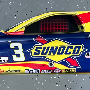 May include: A blue and yellow race car door with the number 3 and the word "SUNOCO" in large yellow letters. The door also has several sponsor logos, including "Delphi", "Total", "BBS", "Fuel Safe", and "Earl's".