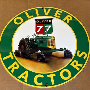 May include: A round metal sign with the words "Oliver Tractors" in a circle around a green tractor with the words "Oliver 77" on the side.