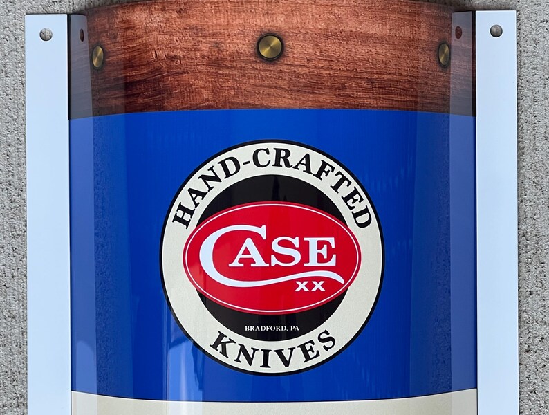 May include: A blue and white sign with a red circle containing the text "Case XX" and the words "Hand-Crafted Knives" around the circle. The sign has a woodgrain border.