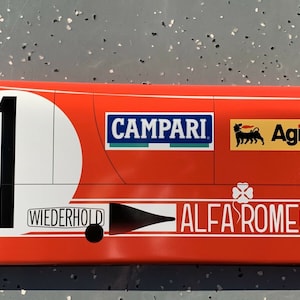 May include: A red, white, and black race car replica with the number "1" on the side. The car has sponsors including "Campari", "Agip", and "Wiederhold". The car is labeled "Alfa Romeo".
