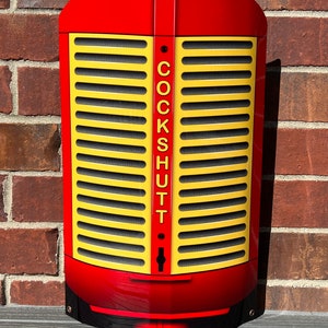 May include: Red metal tractor grill with a yellow grill and the word "COCKSHUTT" in black lettering.