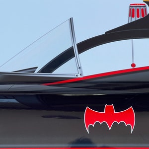 K&ouml;nnte beinhalten: Ein schwarzer und roter Batmobil mit einer klaren Windschutzscheibe und einem roten Fledermaus-Symbol an der Seite.