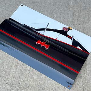 K&ouml;nnte beinhalten: Ein schwarzer und roter Batmobile aus der Batman-Fernsehserie der 1960er Jahre. Das Auto hat ein rotes Fledermaussymbol an der Seite und ein wei&szlig;es Dach. Das Auto befindet sich auf einem wei&szlig;en Hintergrund.