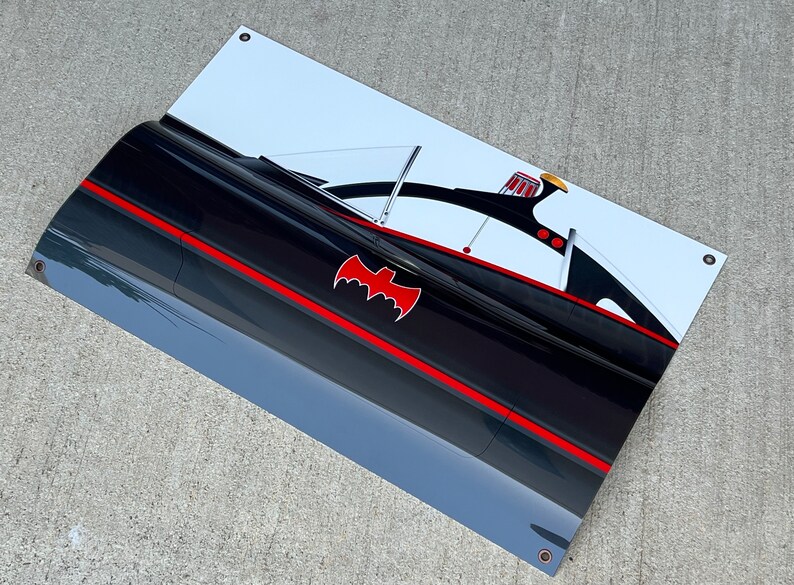 K&ouml;nnte beinhalten: Ein schwarzer und roter Batmobile aus der Batman-Fernsehserie der 1960er Jahre. Das Auto hat ein rotes Fledermaussymbol an der Seite und ein wei&szlig;es Dach. Das Auto befindet sich auf einem wei&szlig;en Hintergrund.