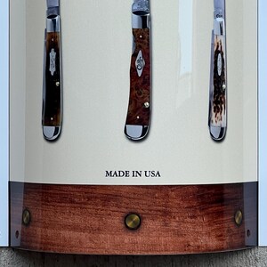 May include: Three pocket knives with wooden handles and silver blades displayed on a wooden background. The knives are arranged vertically and the text "MADE IN USA" is printed below them.