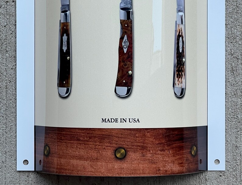 May include: Three pocket knives with wooden handles and silver blades displayed on a wooden background. The knives are arranged vertically and the text "MADE IN USA" is printed below them.